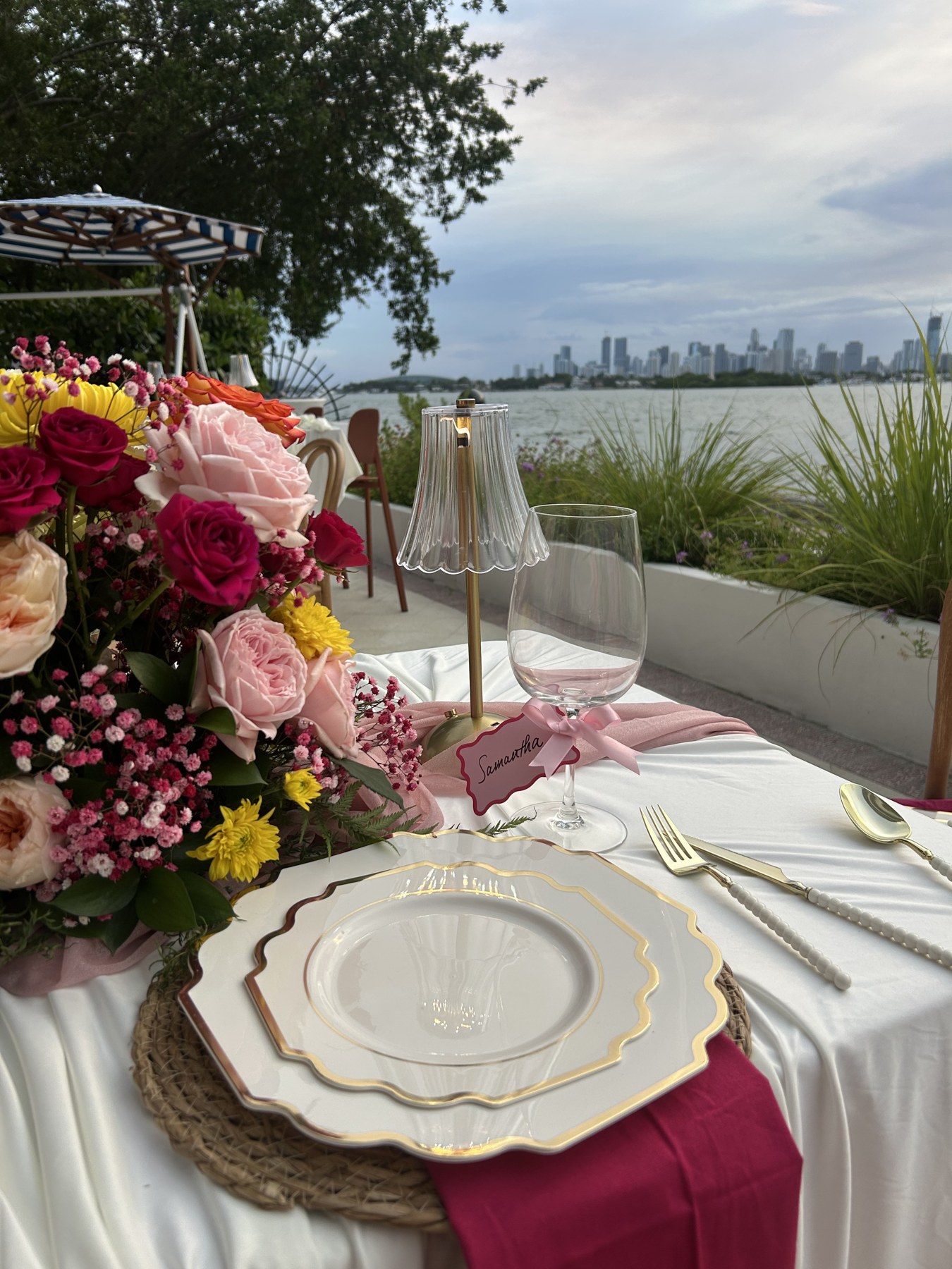 Pink and yellow baby-shower flowers beside a personalized place setting and waterfront views