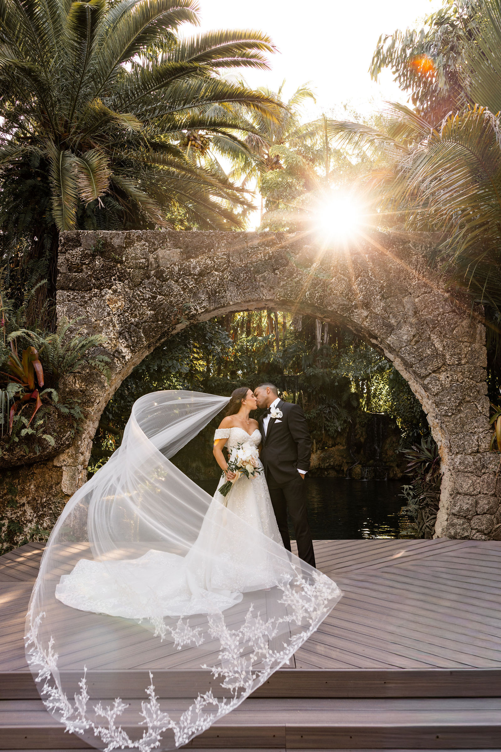 The couple beneath a sunlit tropical stone arch