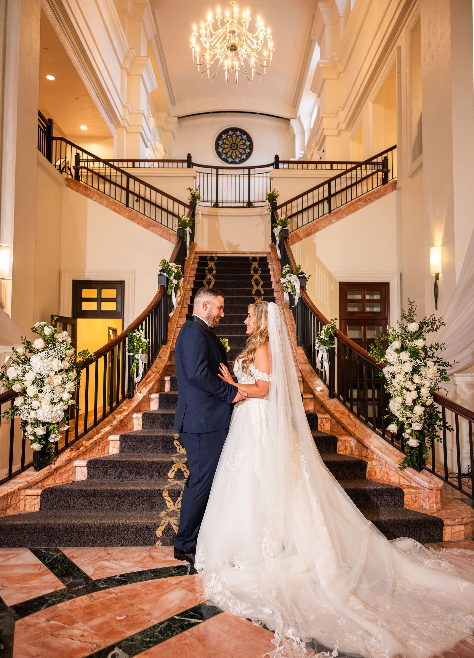 The couple together on a grand staircase framed by white florals