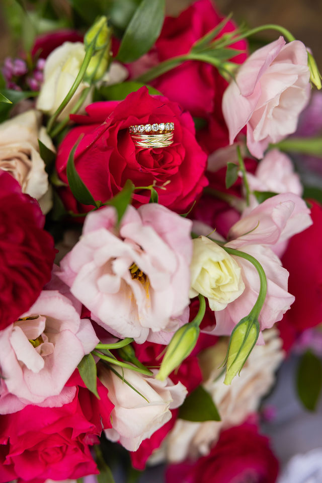 Wedding bands nestled in a bouquet of deep pink roses and blush flowers