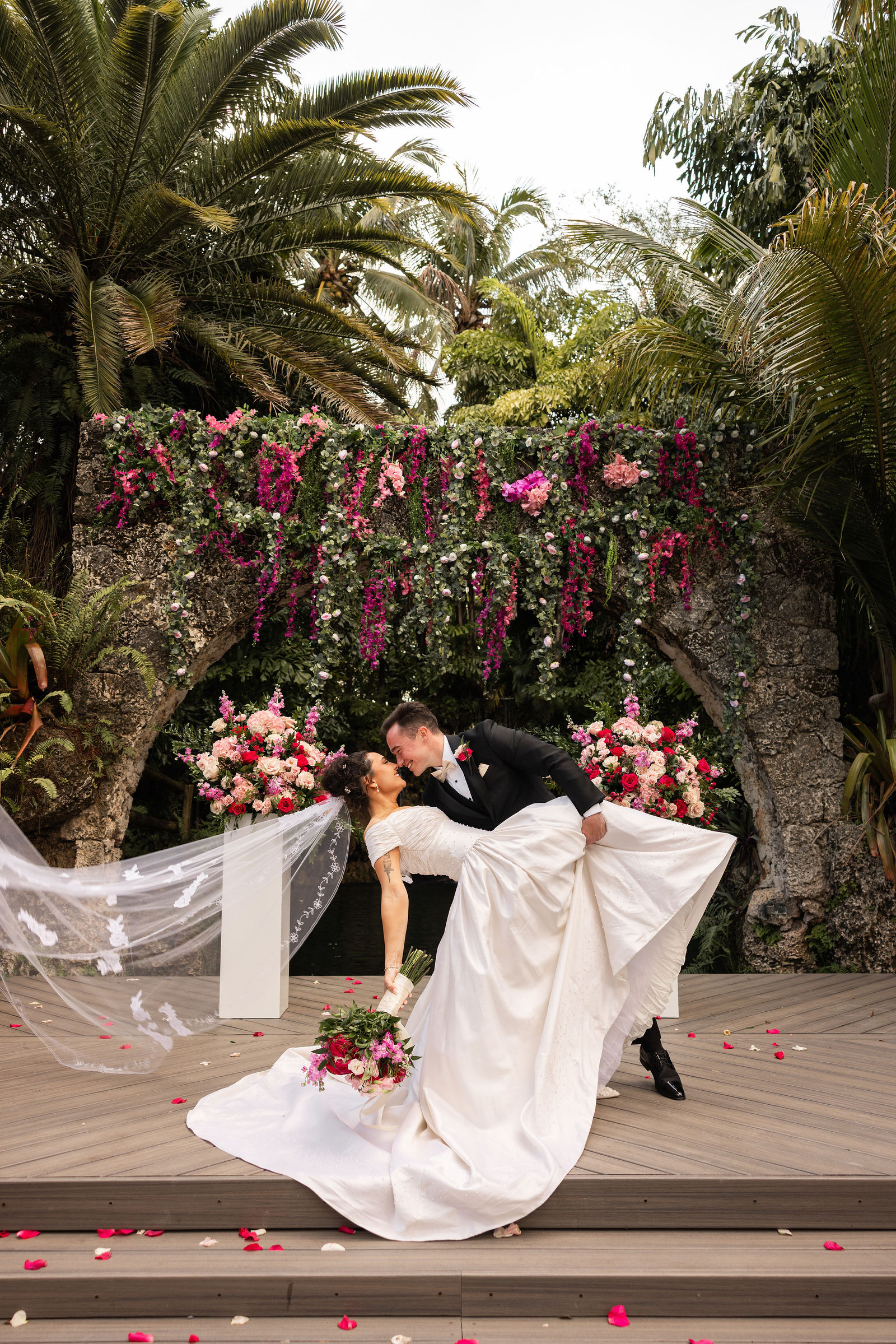 The couple beneath a stone arch decorated with cascading pink florals