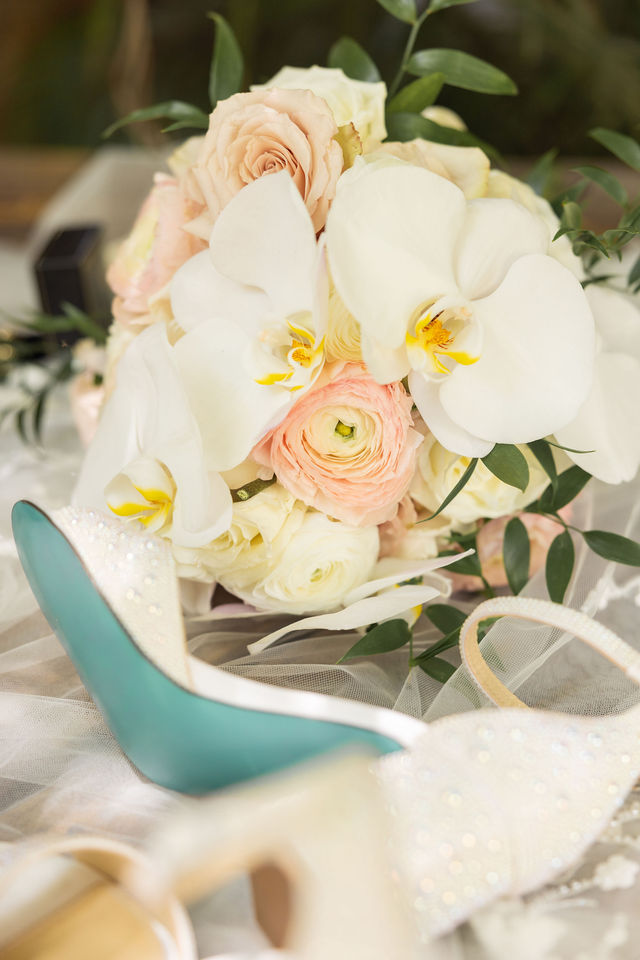 White orchids and blush roses beside sparkling bridal shoes