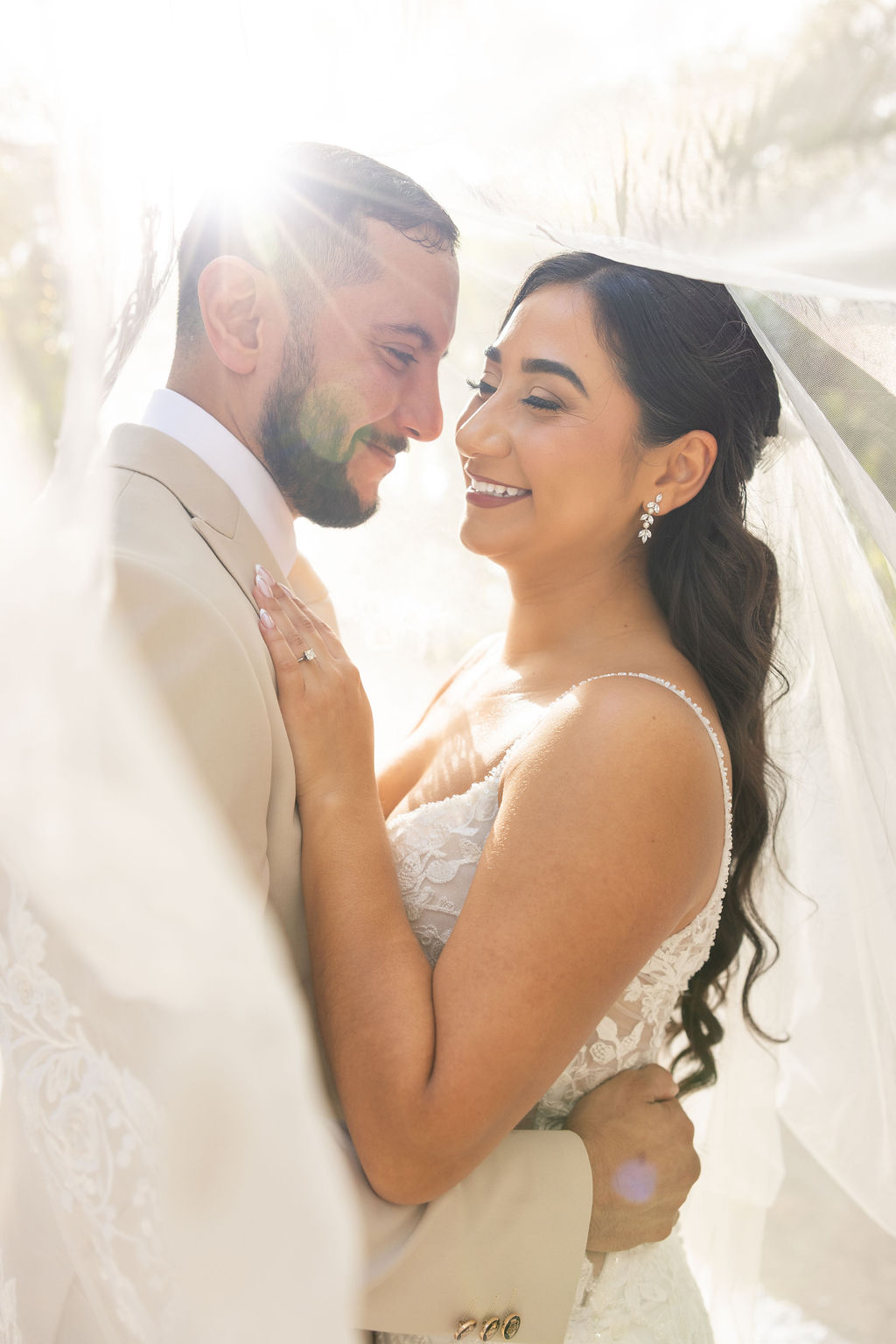 The couple smiling together beneath a wedding veil