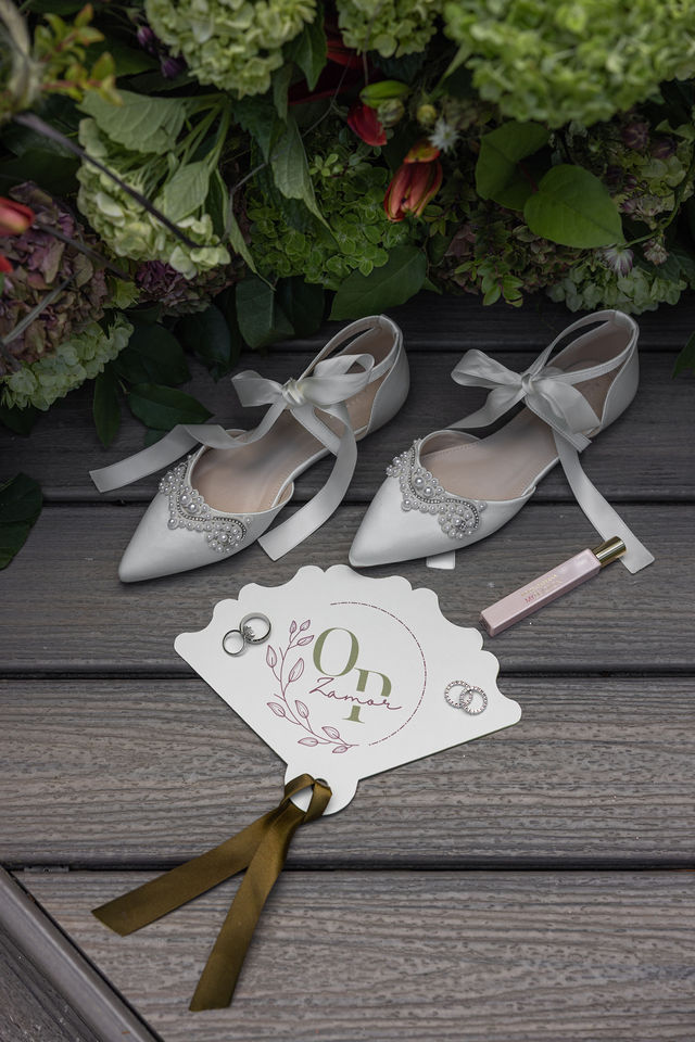 Embellished bridal shoes and wedding rings beside lush florals
