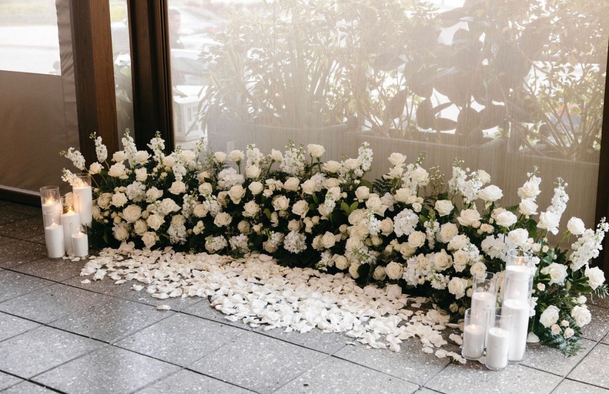 White floral installation with candles and scattered petals