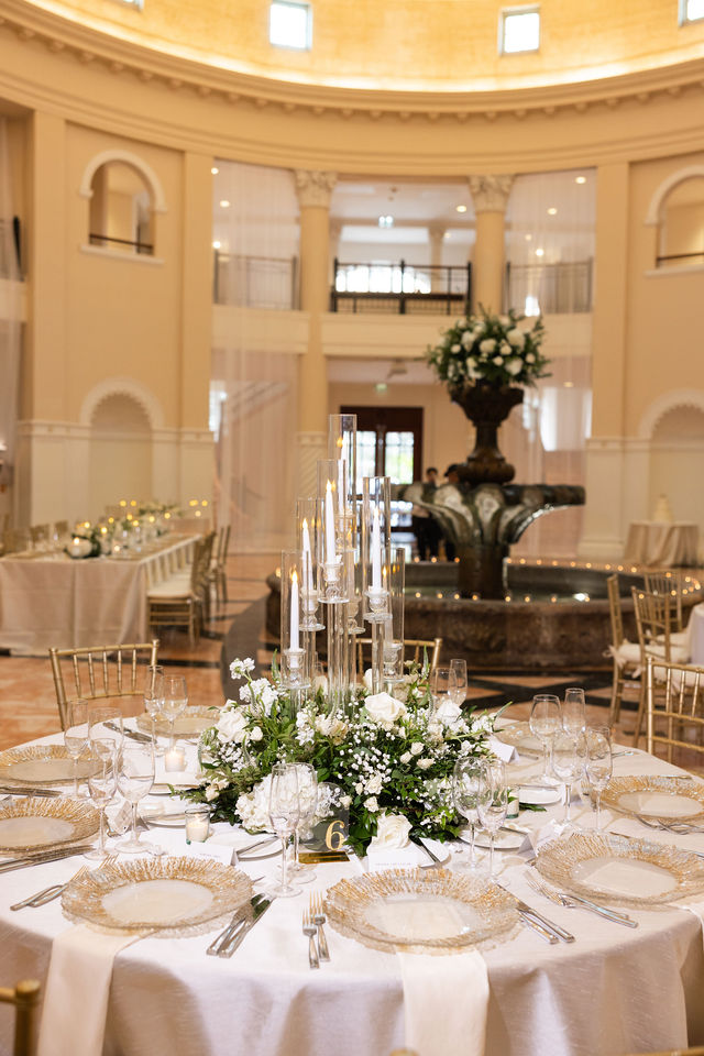 White floral centerpieces and gold place settings in a grand reception room