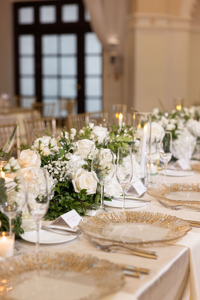 An elegant tablescape with white roses, gold chargers and crystal glassware
