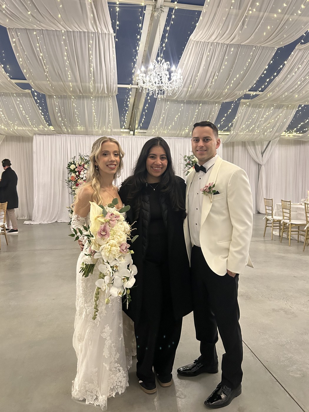 An event planner with a newlywed couple beneath draping and twinkle lights