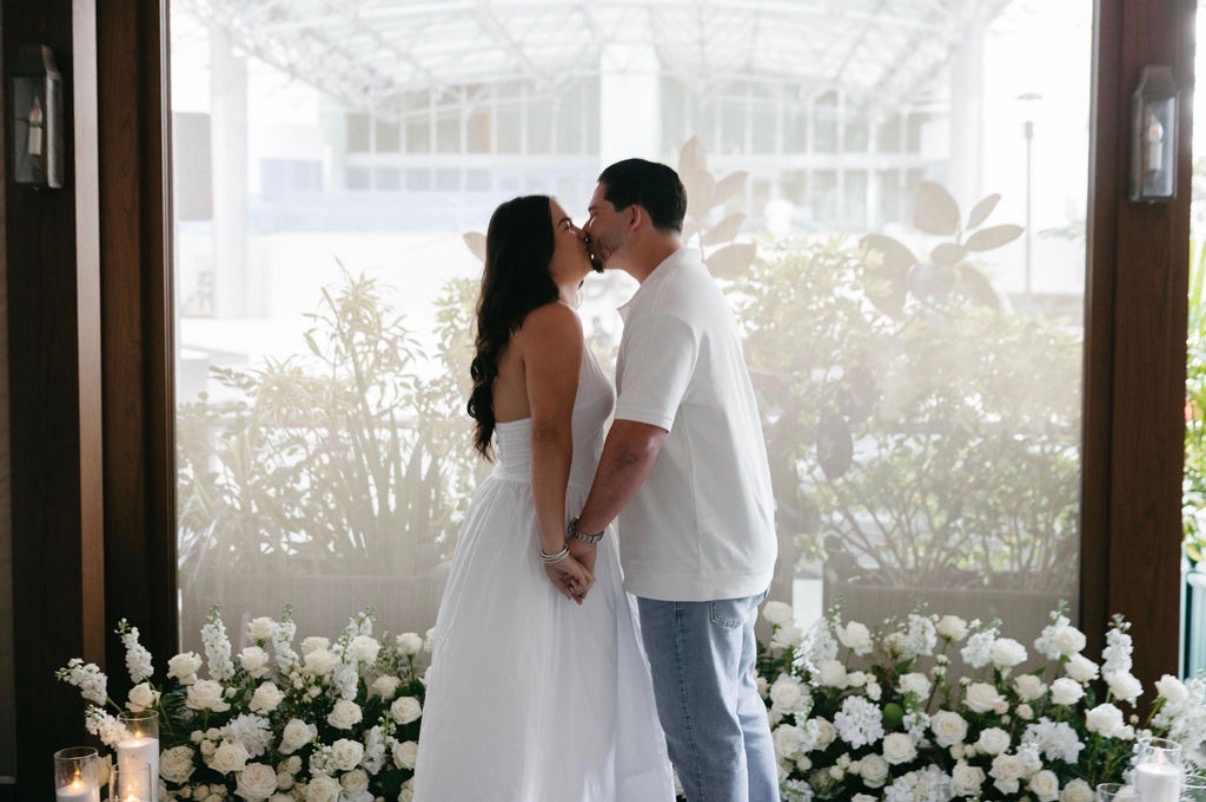 A couple kissing in front of white flowers after their proposal