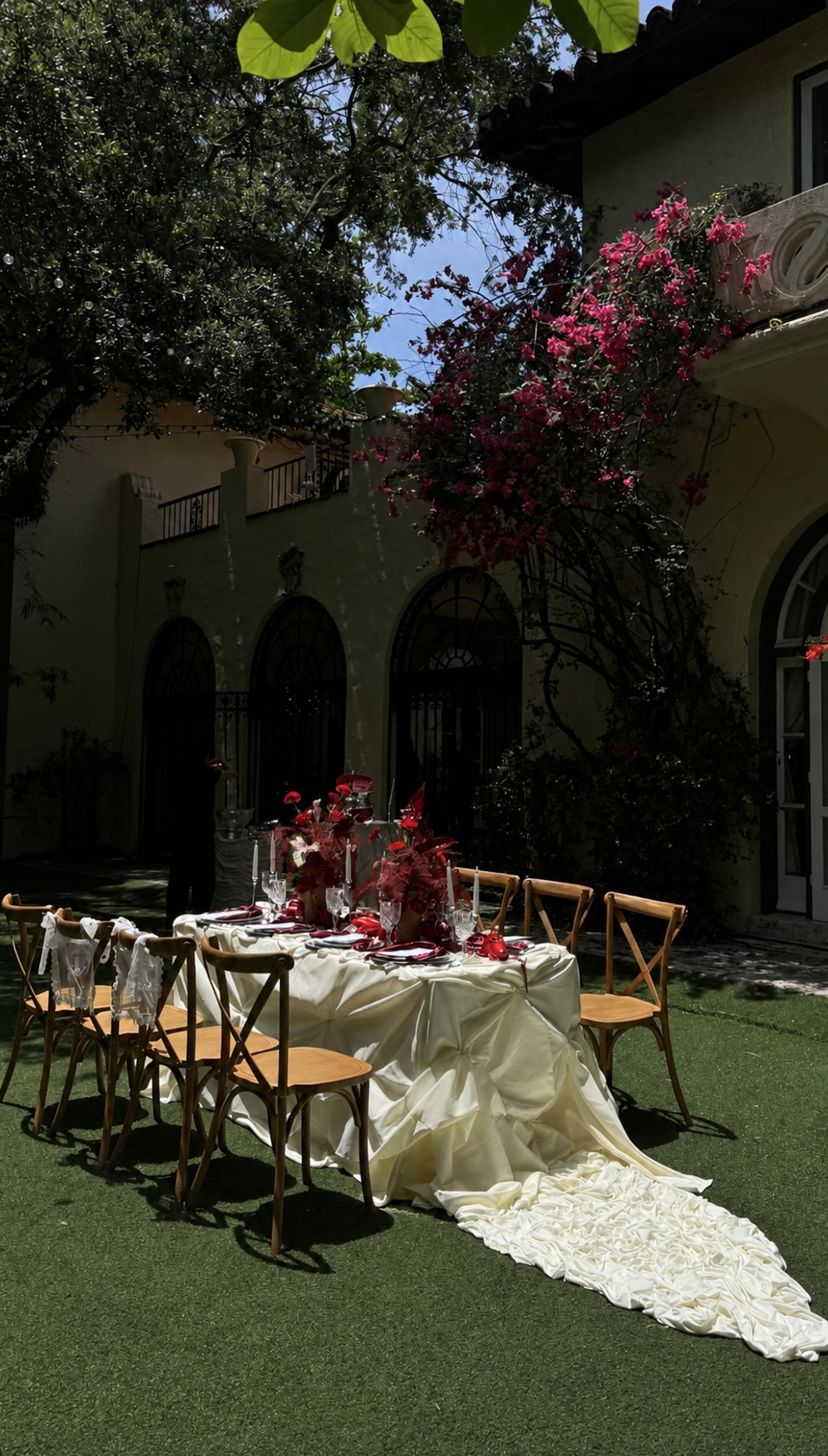 An ivory-draped table with berry flowers in a sunlit garden courtyard