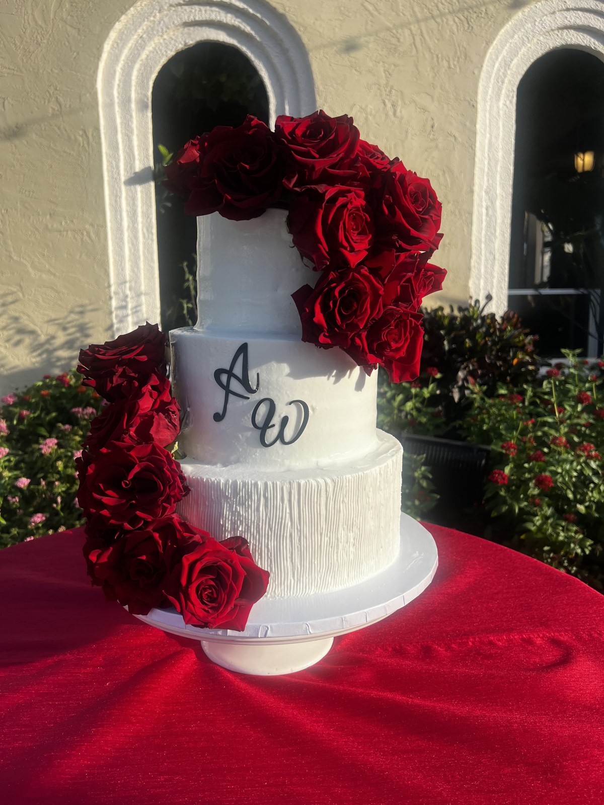 A white tiered wedding cake decorated with cascading red roses